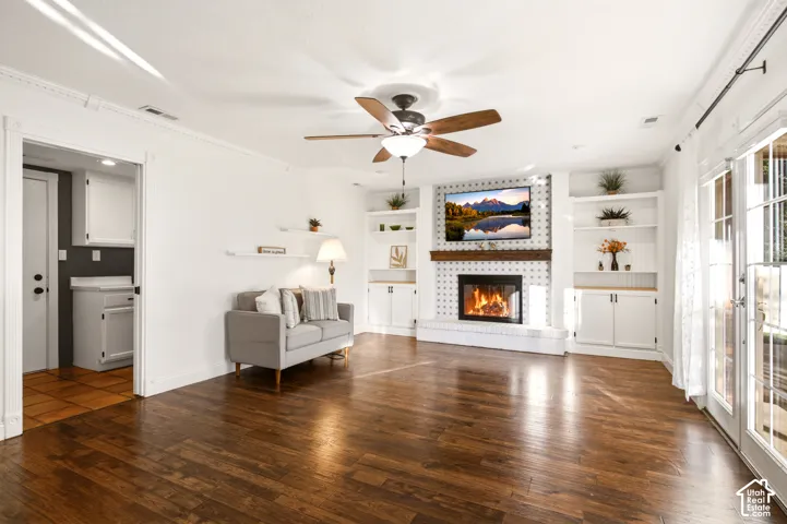 Living area featuring wood-finish flooring, fireplace with a wood mantel, built-in cabinetry, crown molding, and glass-paneled sliding doors