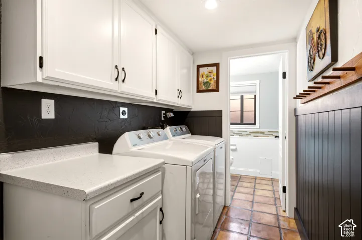 Laundry room featuring white cabinetry, textured dark backsplash, matte black hardware, vertical wainscoting, and ceramic tile flooring
