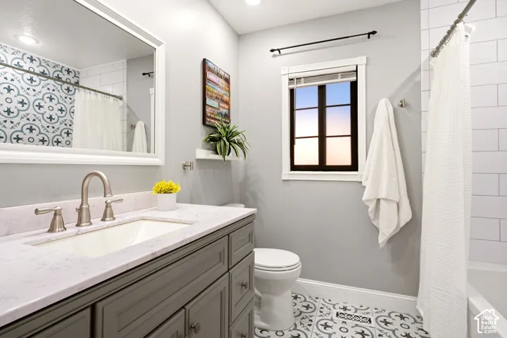 Vanity featuring grey cabinetry, a quartz countertop with an integrated rectangular sink, and brushed-nickel fixtures, complemented by patterned floor tile, a tiled shower surround, and a framed mirror