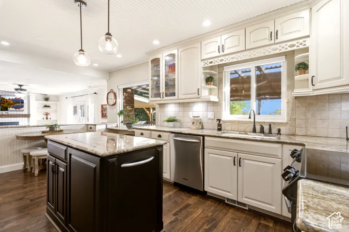 Kitchen featuring a contrasting dark wood center island, custom off-white cabinetry, stone-finish countertops, tile backsplash, and wood-finish flooring