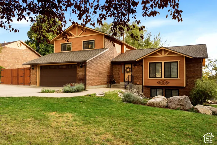 Multi-level exterior featuring a brick and horizontal siding facade, asphalt shingle roof, attached two-car garage, and landscaped front yard with decorative boulders