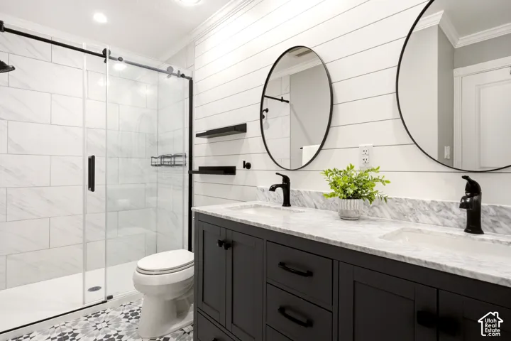 Dual vanity featuring dark cabinetry, stone-finish countertops, matte black fixtures, white horizontal wall paneling, and a glass-enclosed shower with tiled surround