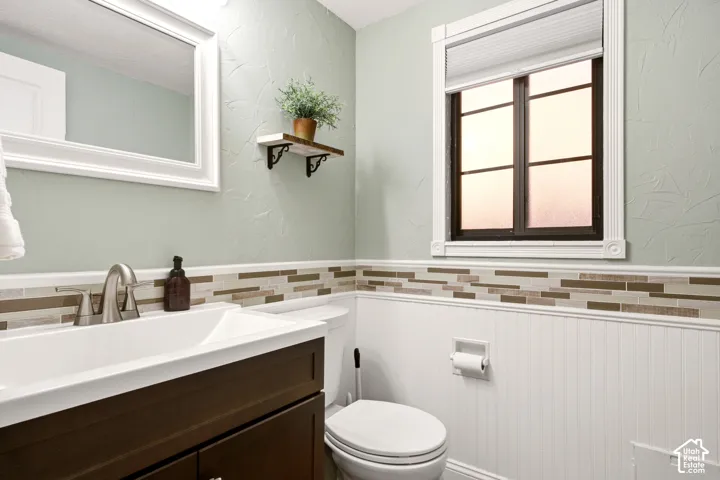 Bathroom featuring a dark wood-finish vanity, white rectangular sink, multi-tonal glass tile backsplash, beadboard wainscoting, and a framed mirror