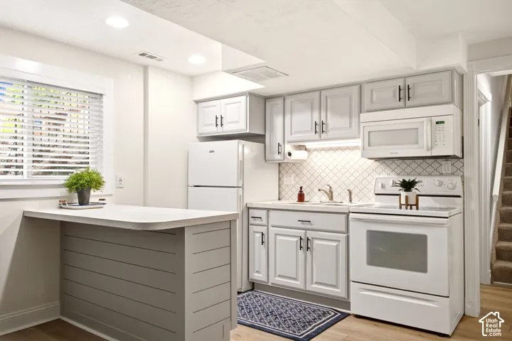 Kitchen featuring light gray shaker-style cabinetry, white appliances, a peninsula with horizontal shiplap detailing, and a neutral diamond-pattern tile backsplash