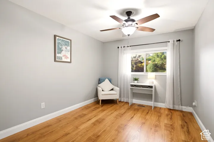 Neutral-toned room featuring wood-finish flooring, a ceiling fan with integrated lighting, and a window with a curtain rod