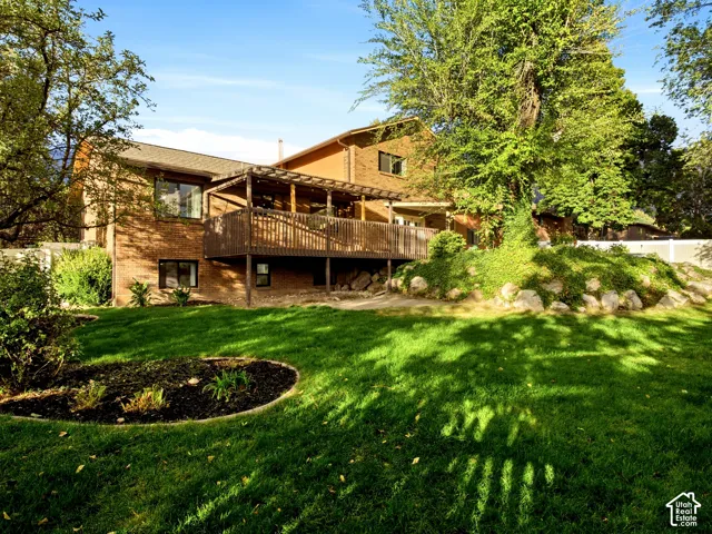Brick exterior residence featuring an elevated wood deck with pergola, stone landscaping elements, and mature trees on the grounds