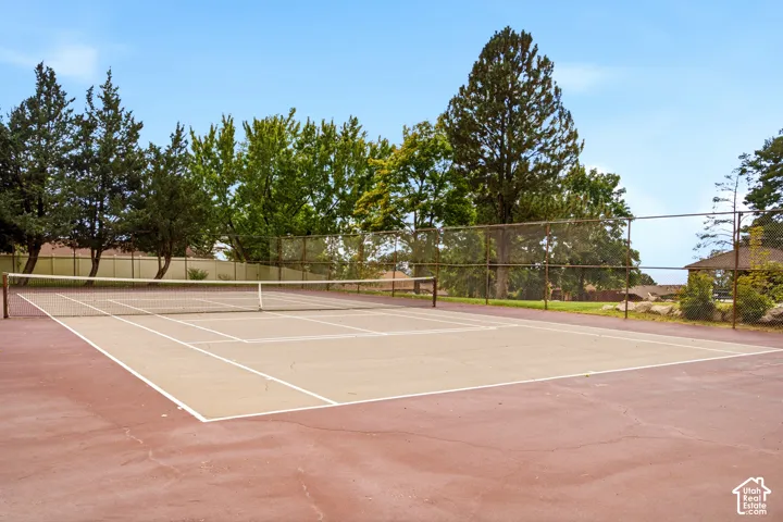 Private tennis court featuring a multi-tone hard surface, perimeter chain-link fencing, and mature perimeter trees