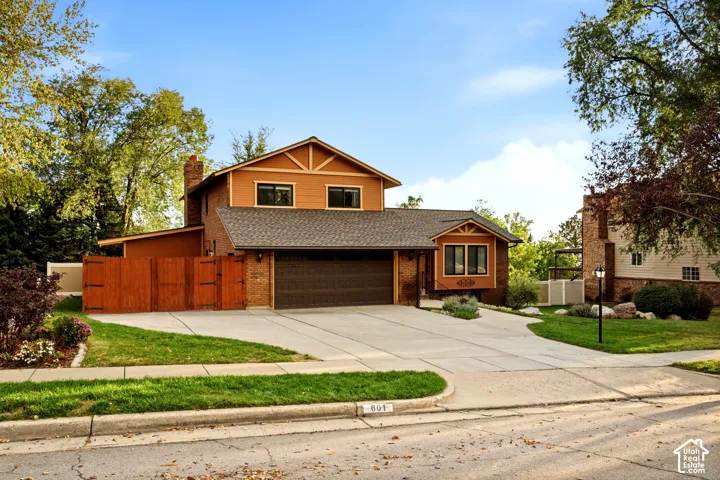 Multi-level exterior featuring a brick and lap siding facade, attached two-car garage, concrete driveway, and solid wood perimeter fencing