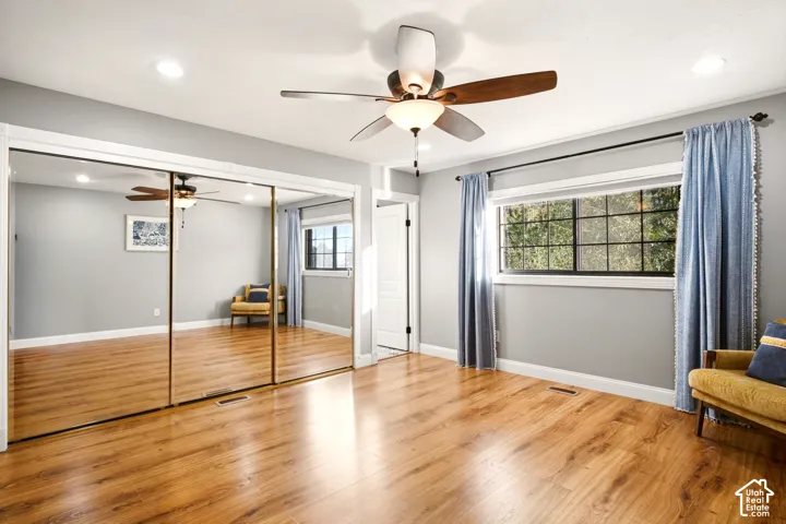 Room featuring wood-finish flooring, recessed lighting, a ceiling fan with integrated light fixture, mirrored sliding closet doors, and grid-pane windows