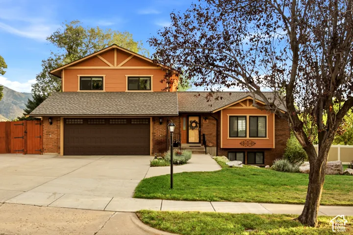 Multi-level exterior featuring a brick and horizontal siding facade, asphalt shingle roof, two-car garage, and concrete driveway