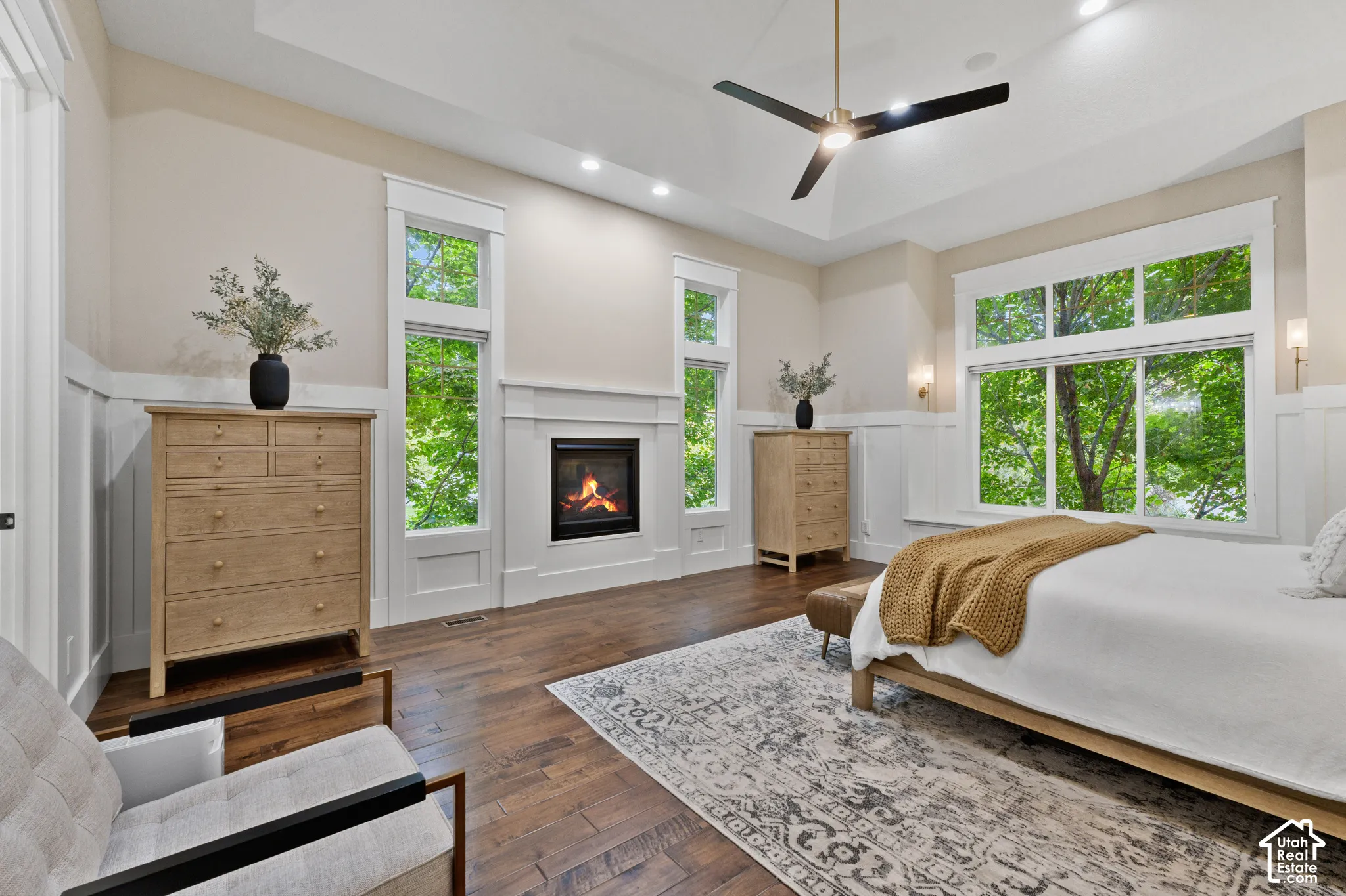 Tray ceiling with integrated recessed lighting, wood-finish flooring, built-in fireplace, wall paneling, and expansive windows