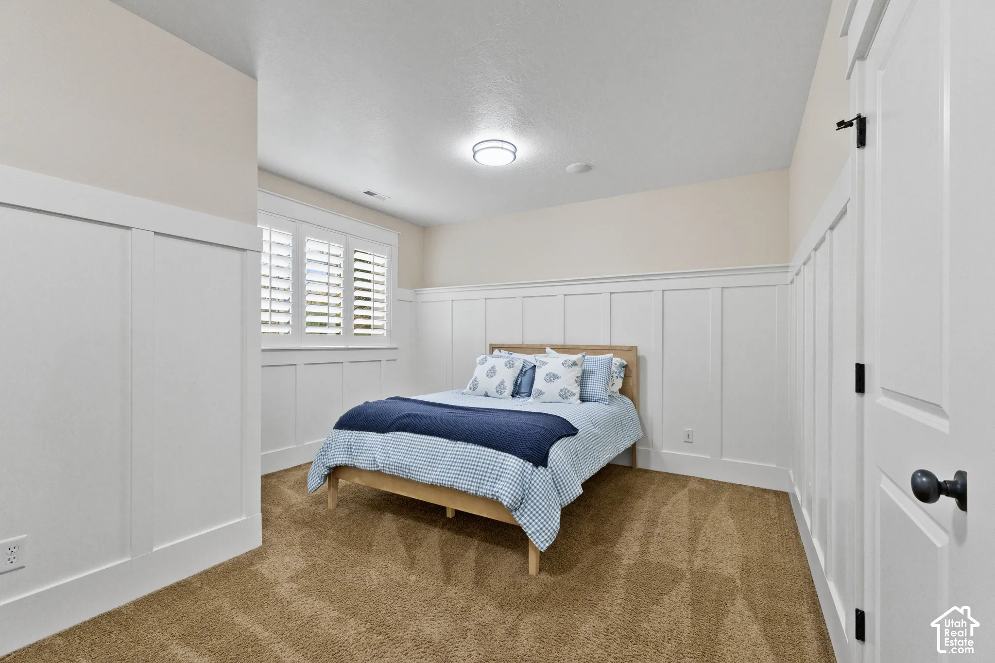 Interior space featuring floor-to-ceiling white board-and-batten wainscoting, wall-mounted shutter treatments, neutral carpeting, and a flush-mount ceiling light fixture