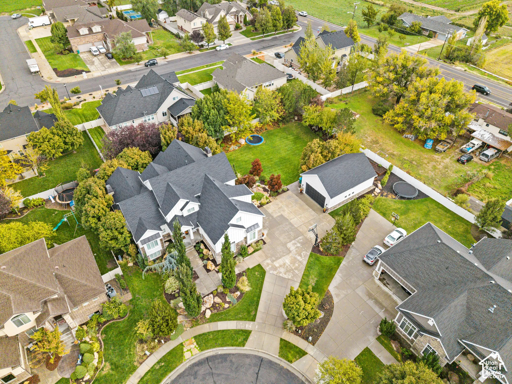 Aerial perspective of a detached multi-car garage, expansive manicured lawn, concrete driveway, and mature landscaping