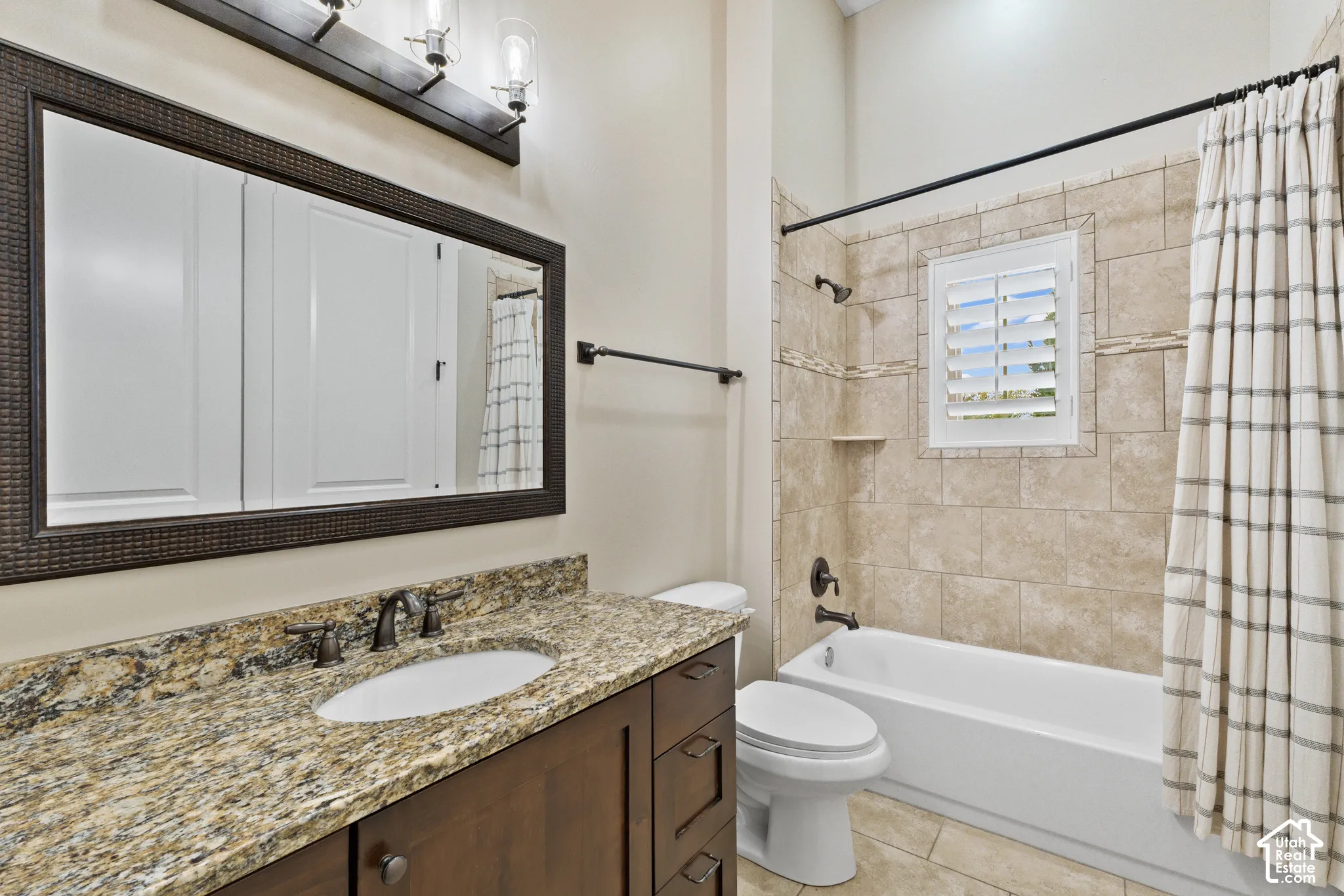 Bathroom featuring a stone-surface vanity with an integrated basin, wood-finish cabinetry, framed wall mirror, three-light fixture, and a tile-surround tub with an inset window