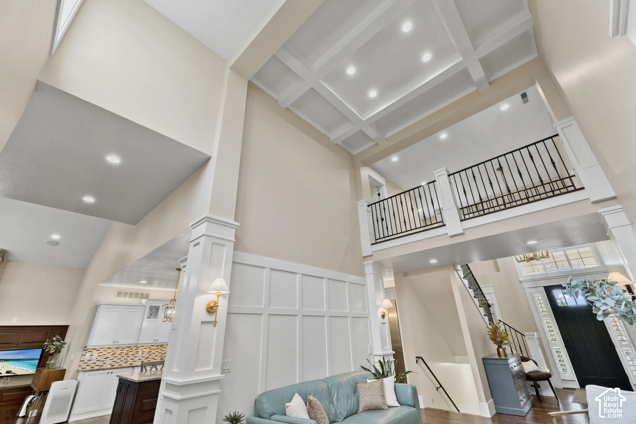 Two-story vaulted ceiling featuring a coffered design, grid-patterned wainscoting, metal railing on the upper level, and built-in wall sconces