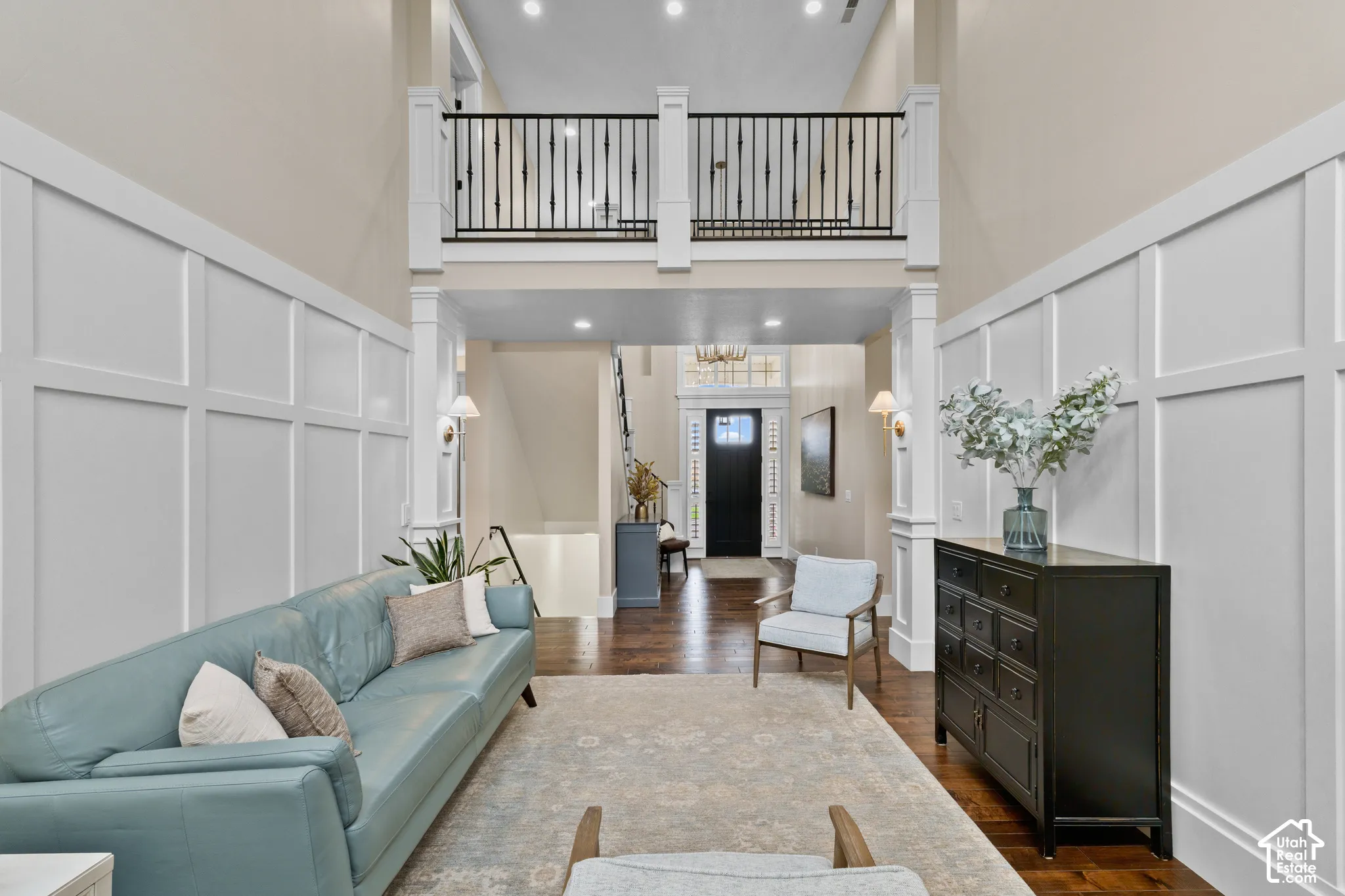 Two-story grand foyer featuring intricate wall paneling, dark wood-finish flooring, a gallery-style metal balustrade, recessed lighting, and a transom-windowed entryway