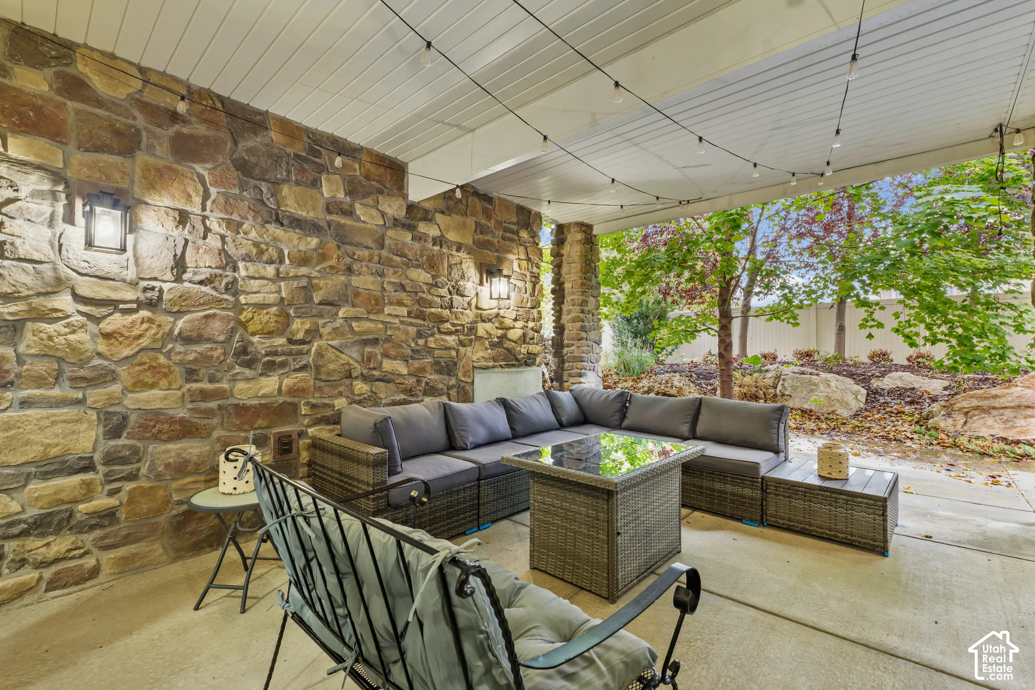 Covered patio featuring a stacked stone accent wall, concrete flooring, and wall-mounted exterior lighting
