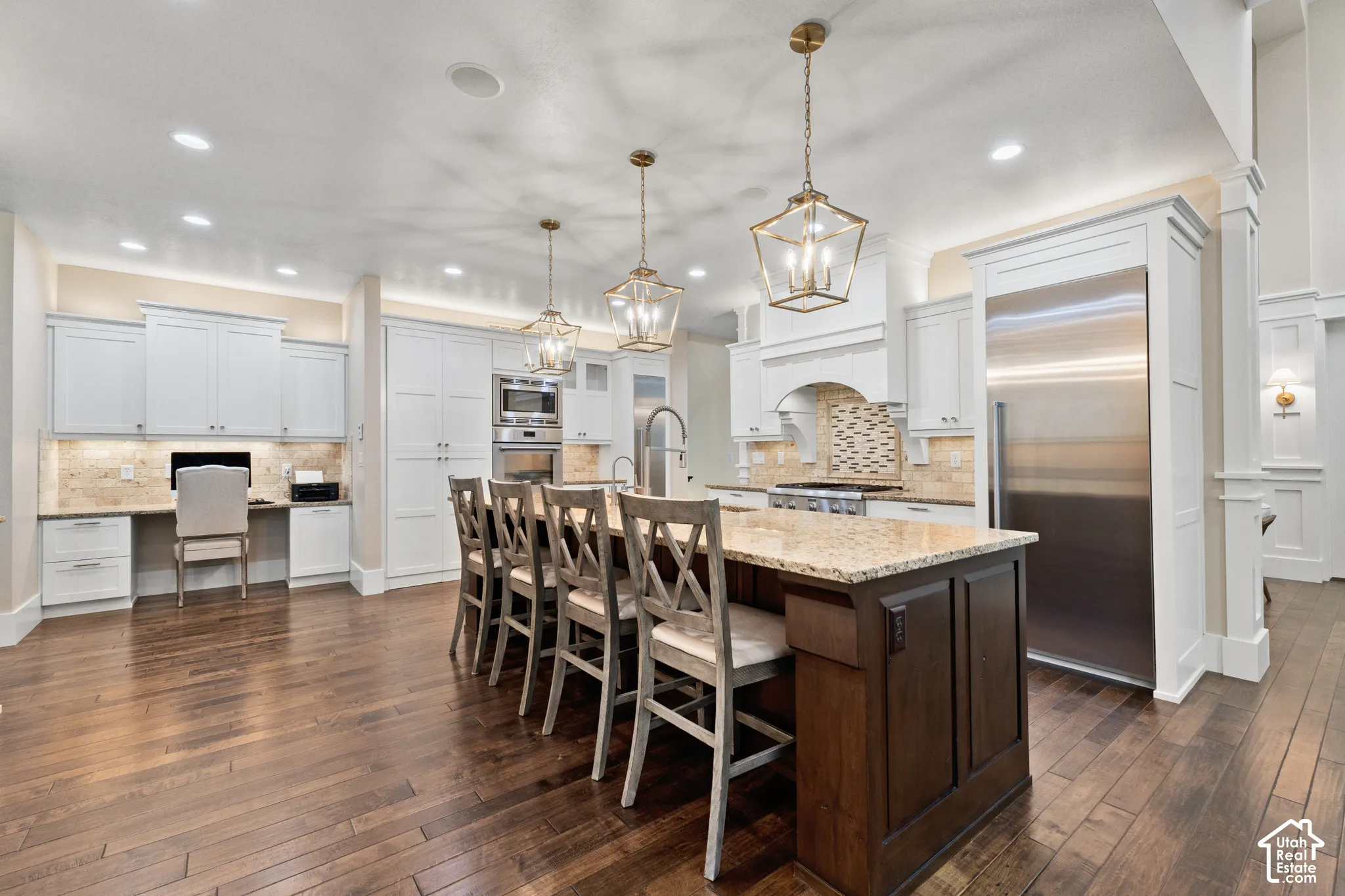 Kitchen featuring a contrasting dark wood center island, stone countertops, white cabinetry, integrated stainless steel appliances, and wood-finish flooring
