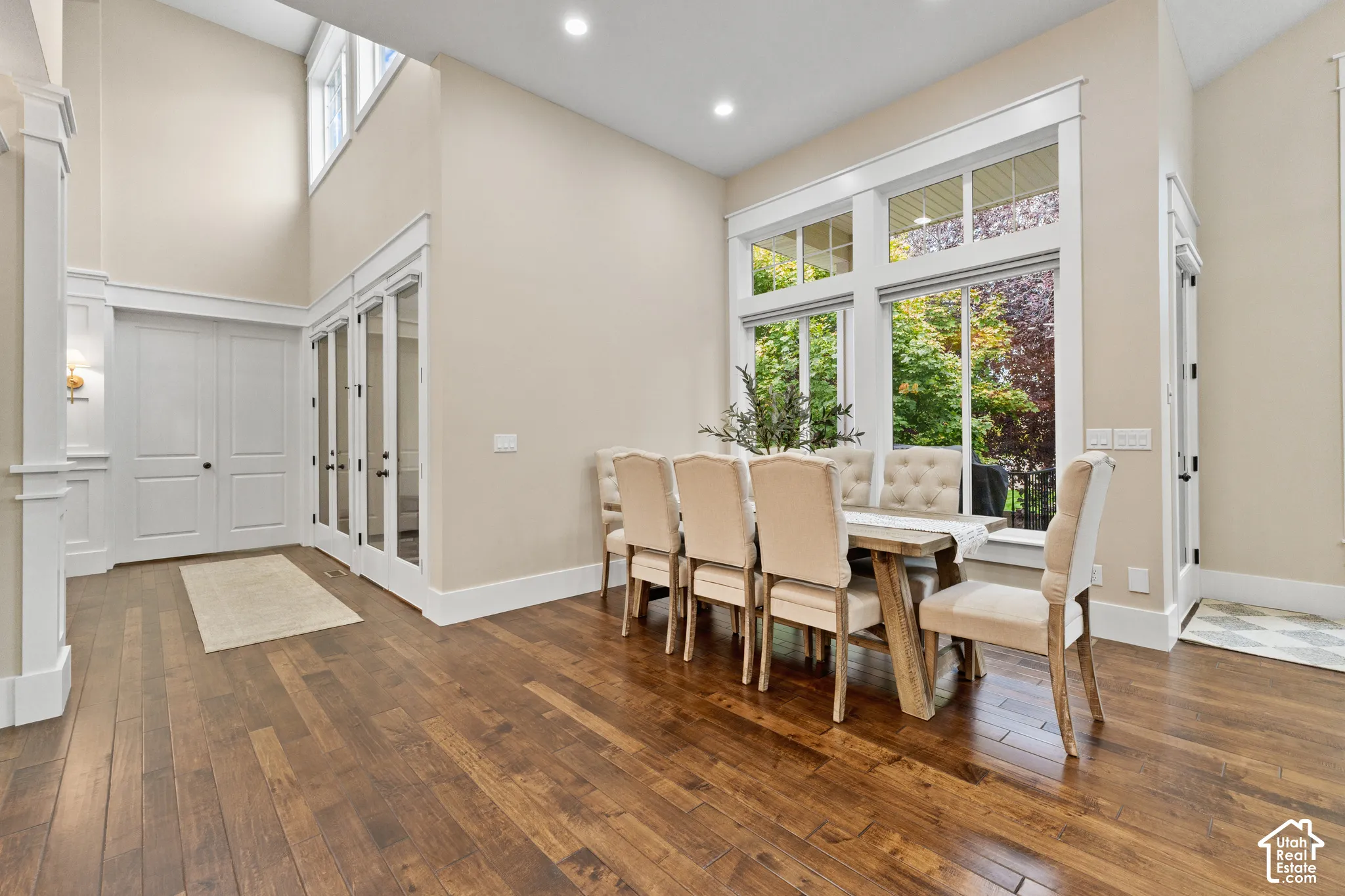 High-ceilinged room featuring wood-finish flooring, recessed lighting, expansive multi-pane windows, and white-framed glass-paneled doors