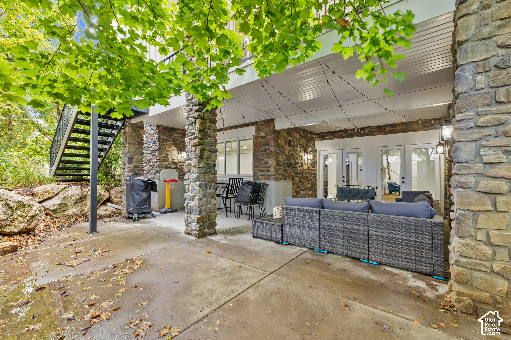 Covered patio featuring stone-clad pillars, concrete flooring, exterior wall-mounted lighting, and a metal staircase