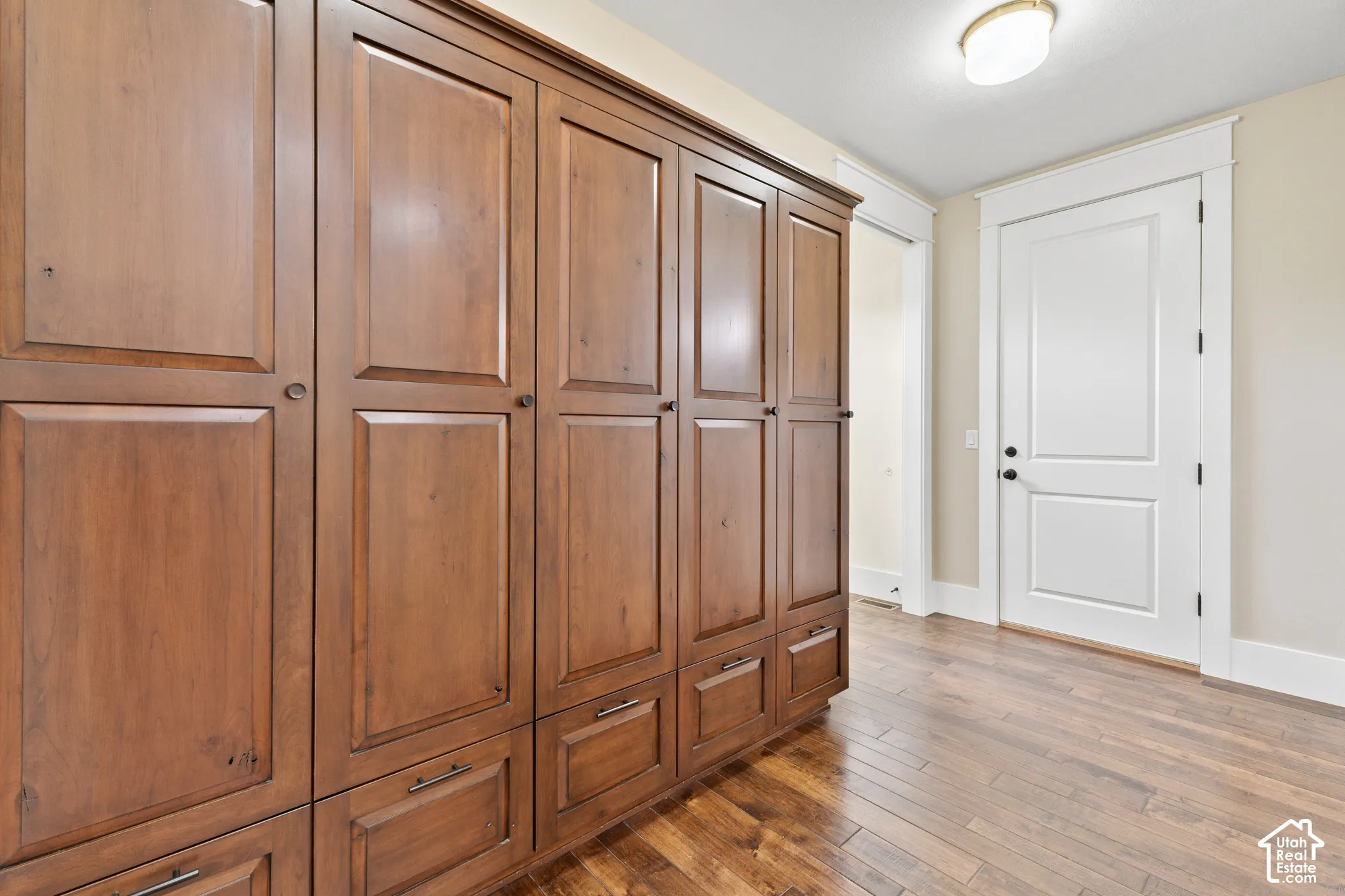 Custom floor-to-ceiling wooden cabinetry with integrated lower drawers, featuring a warm-toned finish and dark metal hardware, complemented by wood-finish flooring and a solid-panel door with architectural door casing