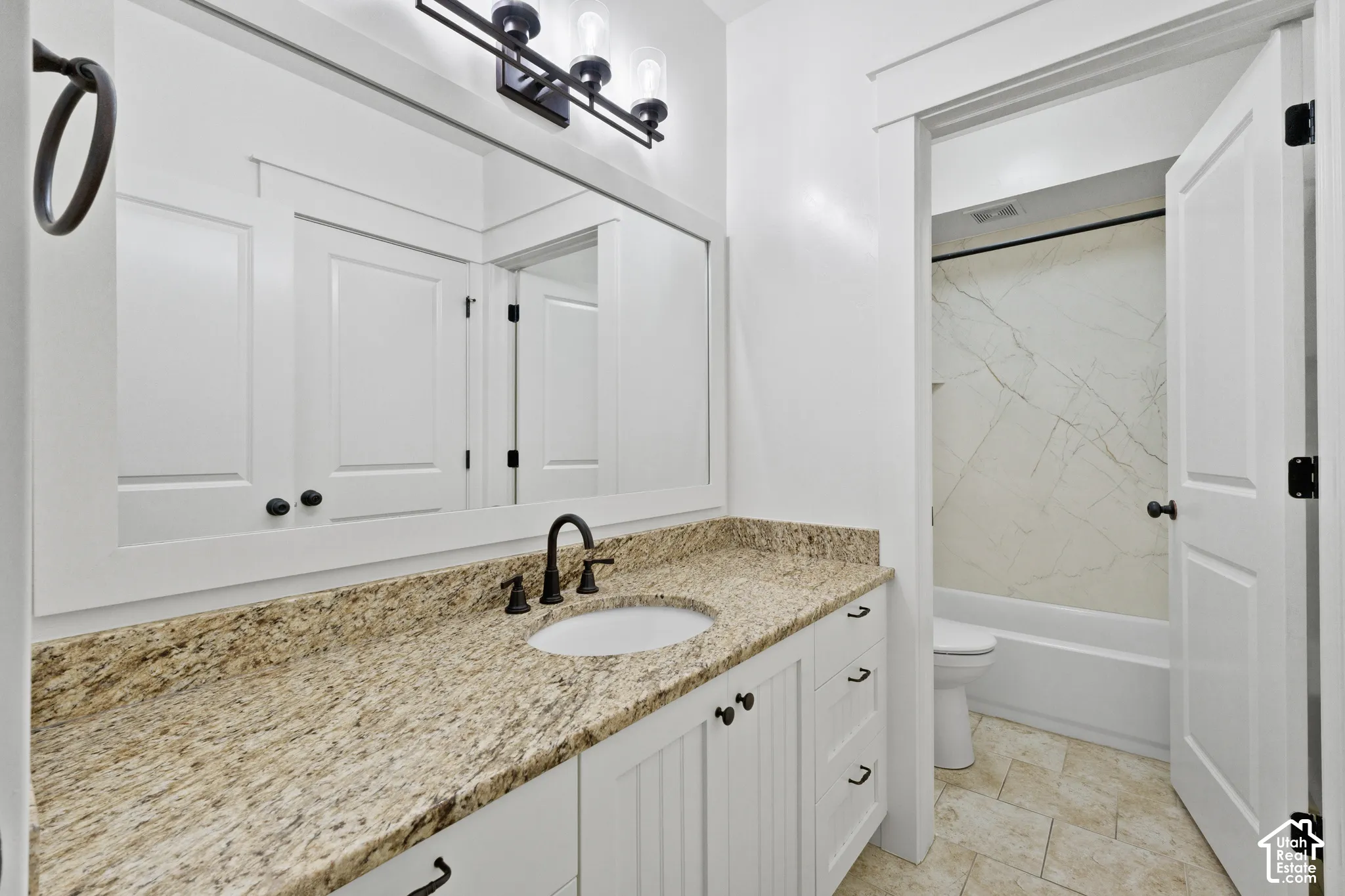Bathroom vanity featuring a stone countertop, white cabinetry, a framed mirror, matte black hardware, and an integrated tub-shower combination with surround tile