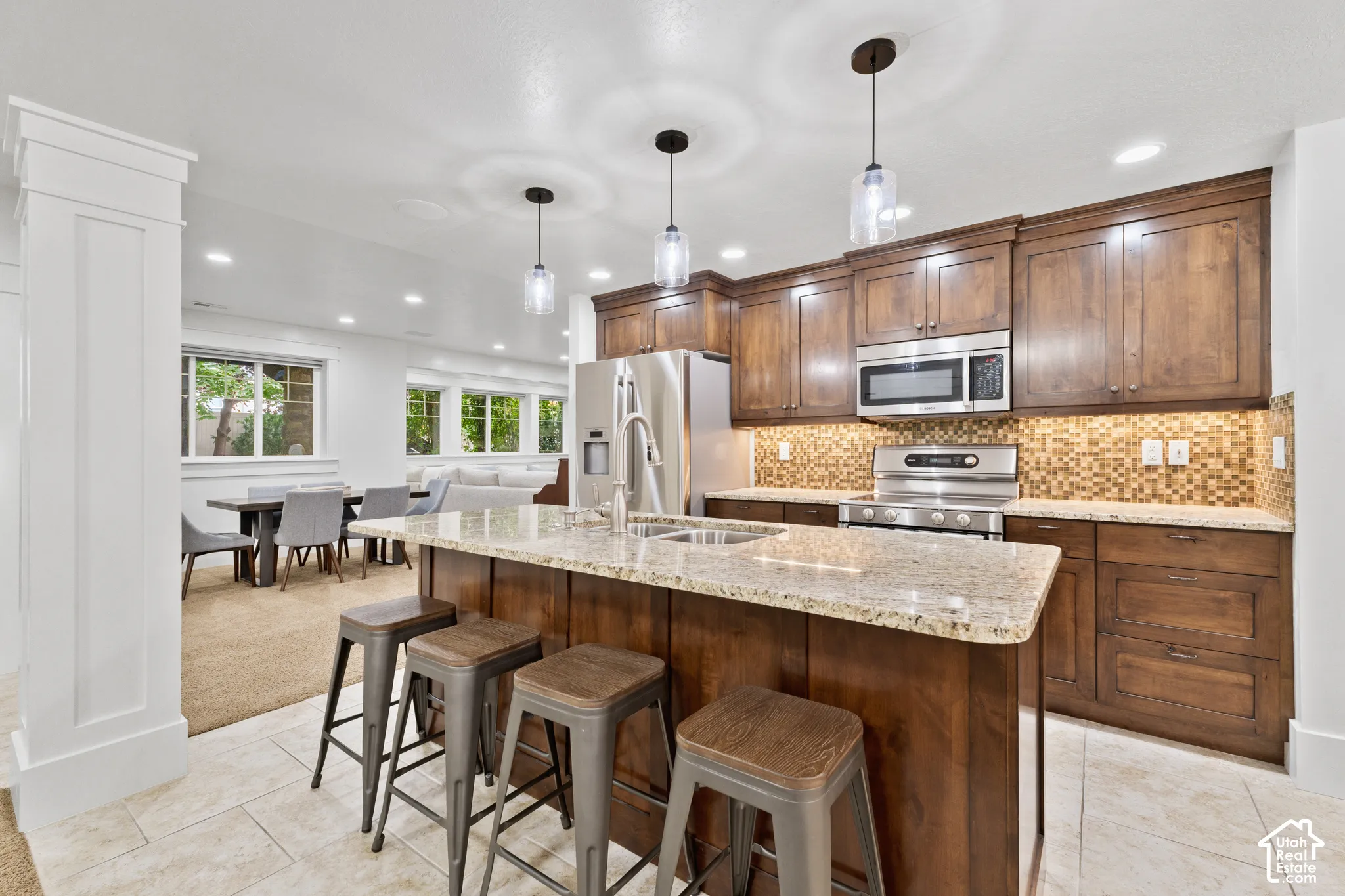 Kitchen featuring wood cabinetry, a central island with a stone countertop, tile backsplash, stainless steel appliances, and pendant lighting