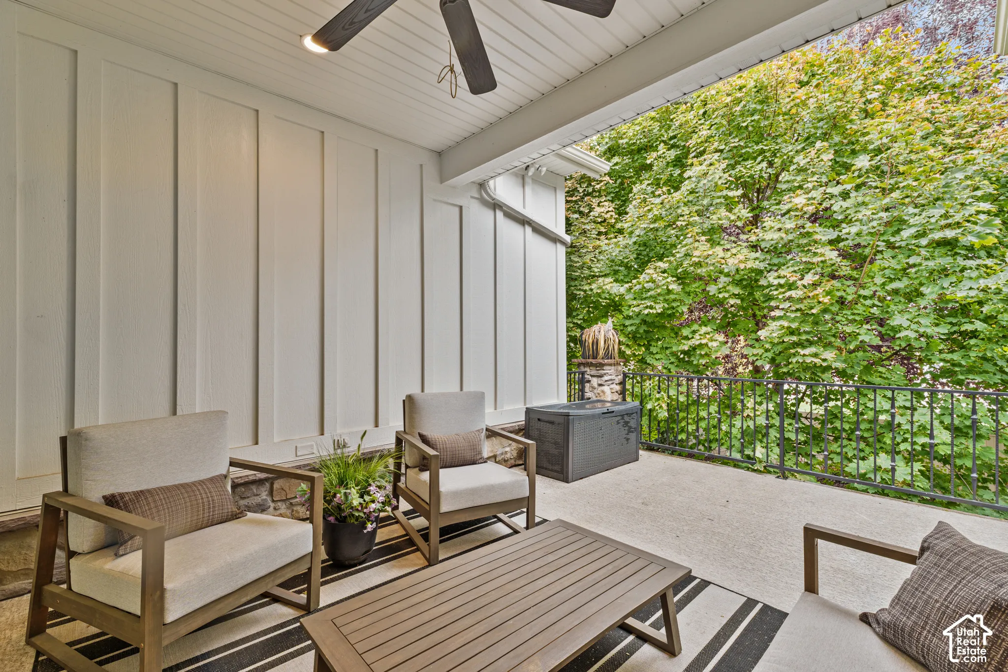 Covered patio featuring board and batten siding, stone masonry accents, a ceiling-mounted fan, and a metal railing