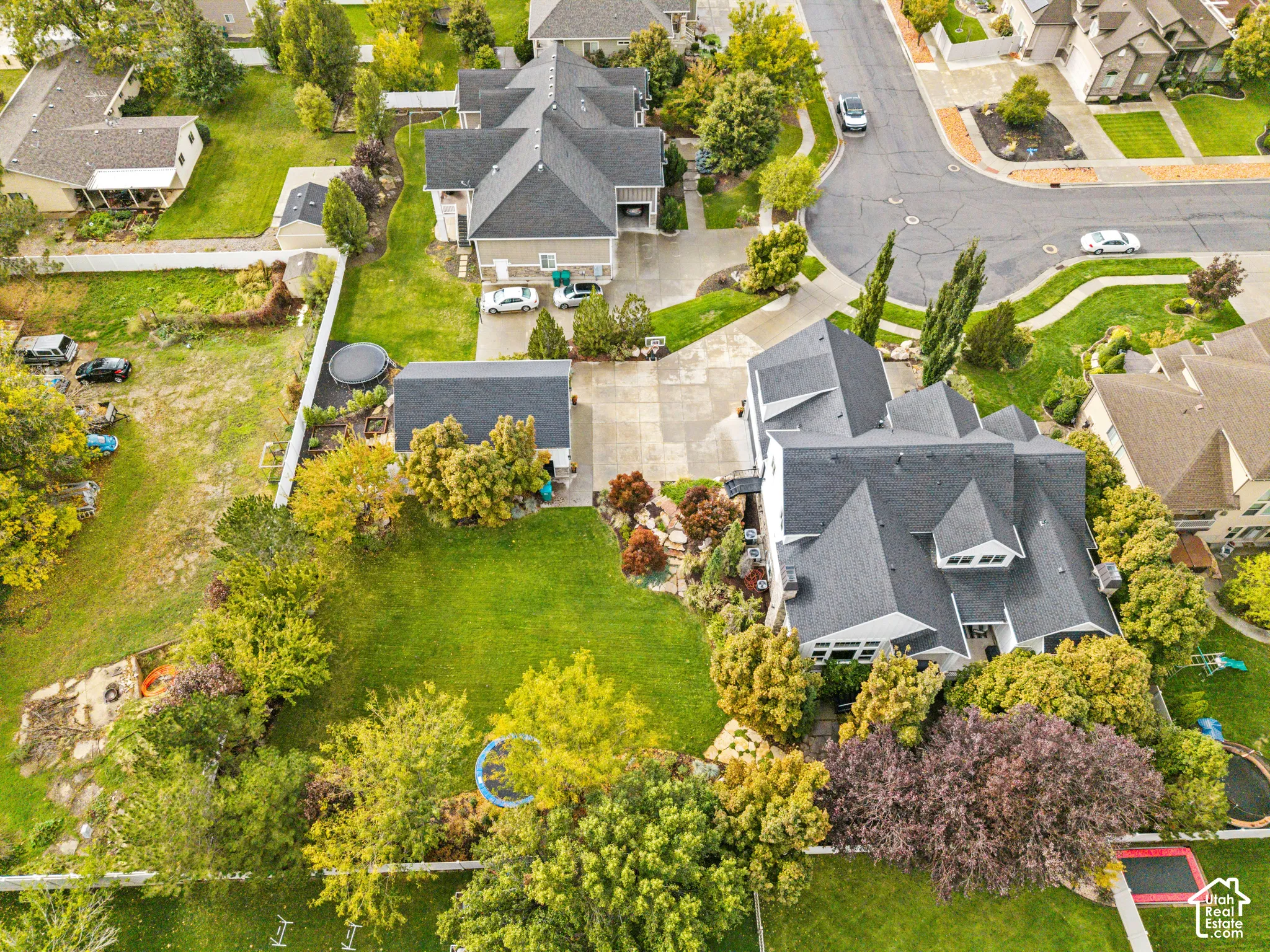 Aerial perspective of a multi-level residence featuring an expansive lawn, concrete driveway, stone hardscaping, and mature trees on a corner lot