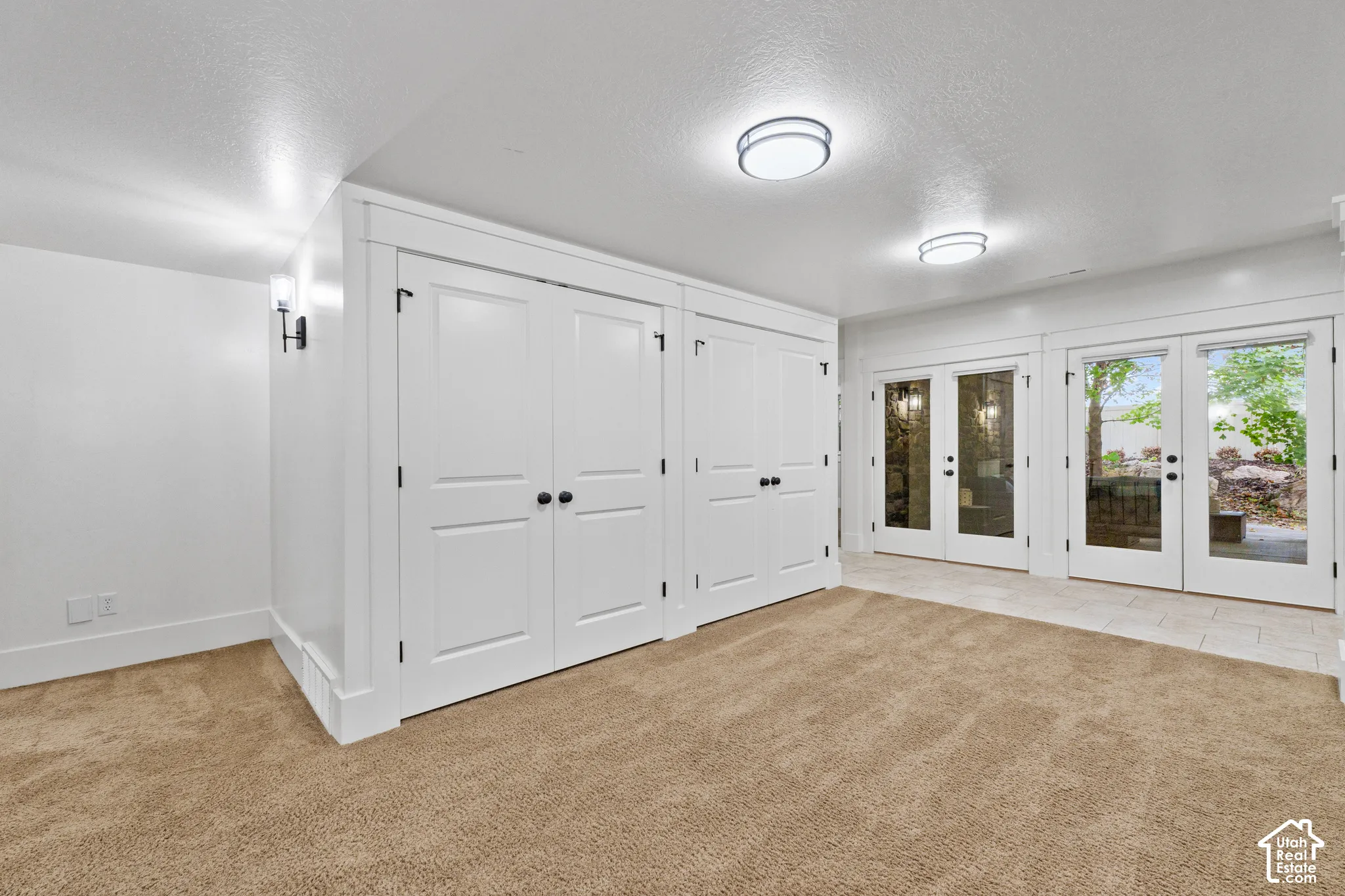 Interior space featuring double French doors with glass panes, wall-to-wall carpeting, dual sets of white shaker-style built-in cabinetry, and flush-mount ceiling lighting