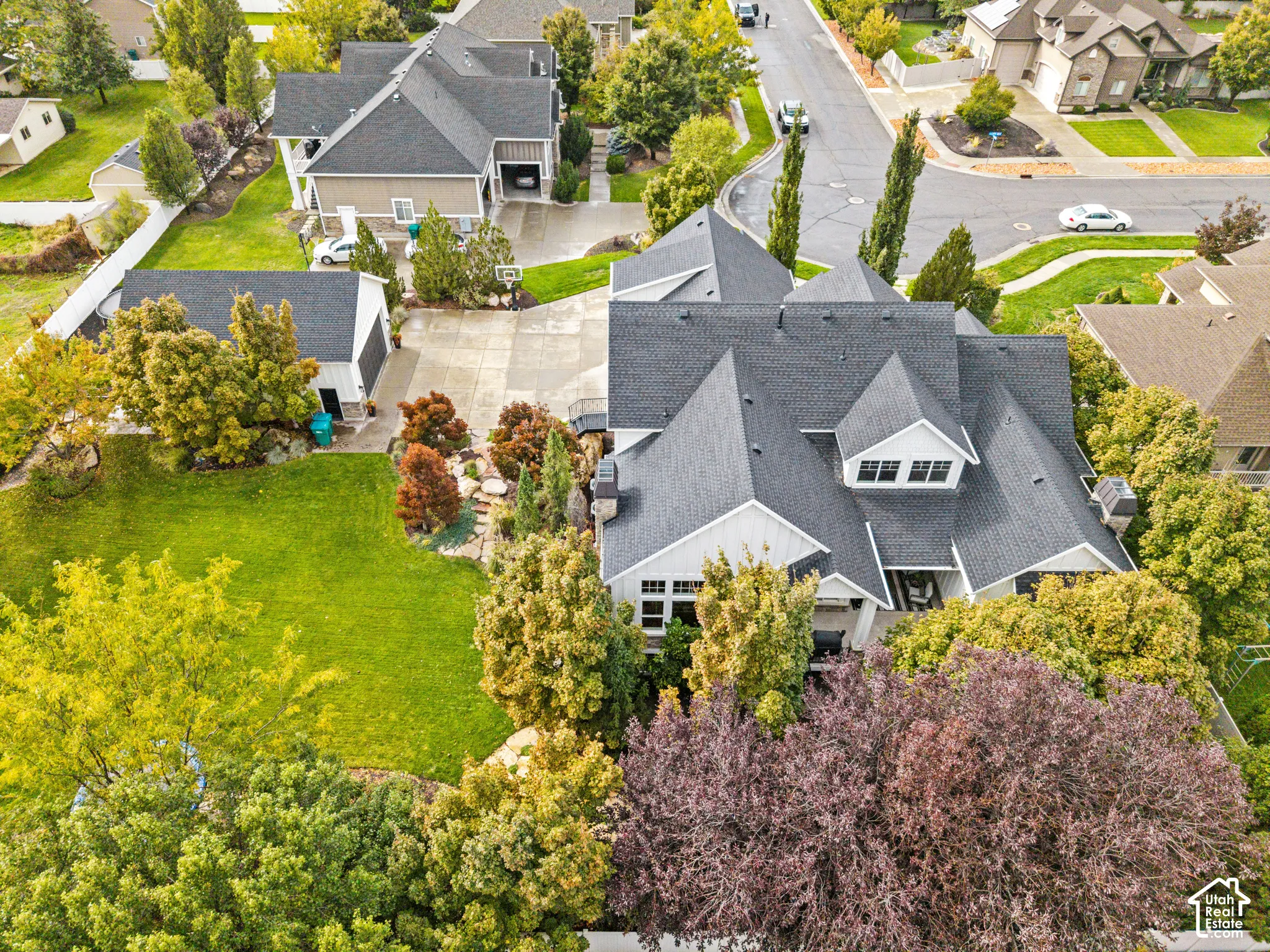 Aerial perspective featuring a multi-gabled architectural roofline, a detached secondary garage, an expansive lawn, and established landscape elements