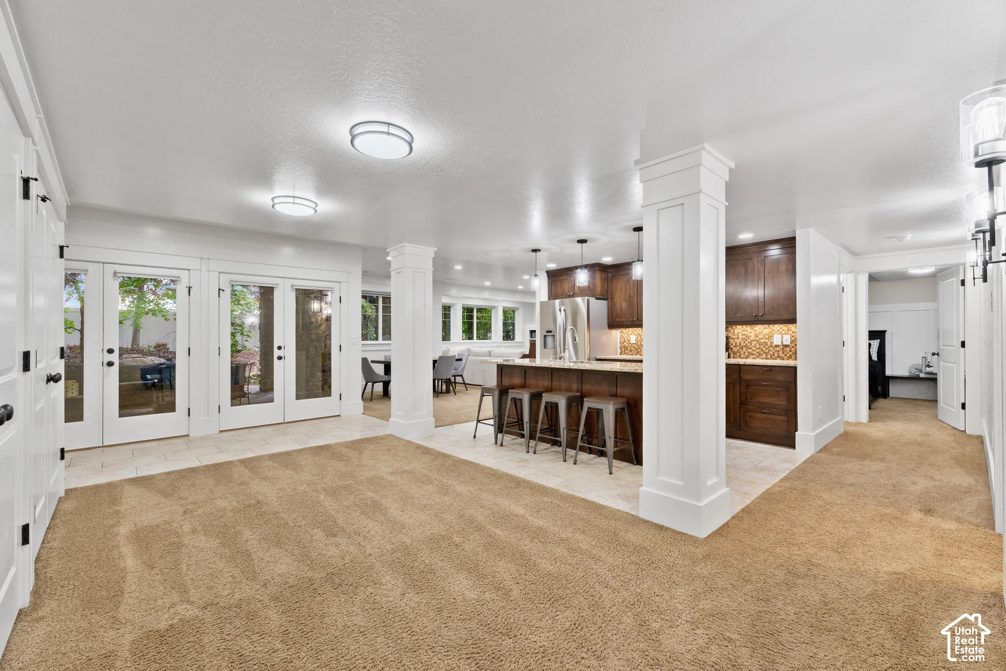 Open-concept interior featuring a kitchen with stained wood cabinetry, stone countertops, a center island, recessed lighting, and double glass doors