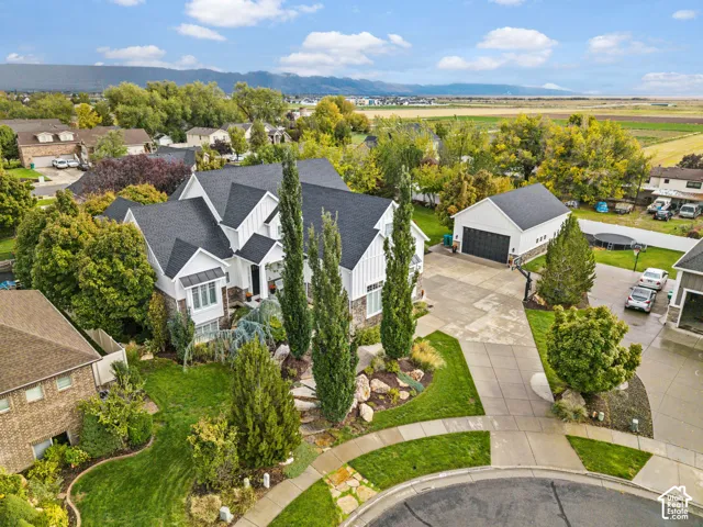 Multi-story residence with board-and-batten siding and stone veneer accents, detached garage, concrete driveway, and professional landscaping set against a mountain backdrop