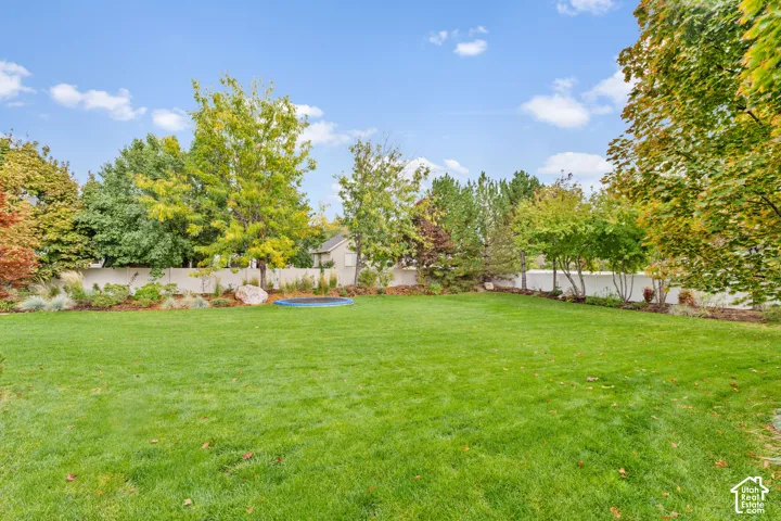 Expansive backyard featuring a level lawn, mature deciduous trees, perimeter privacy fencing, and landscaped garden beds