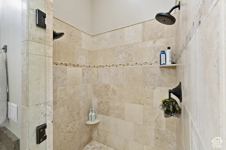 Walk-in shower enclosure featuring large-format stone wall tiles, a decorative mosaic accent border, dual shower heads in a matte black finish, and integrated corner shelving