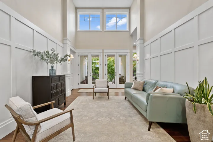 High-ceiling interior featuring dual-level walls with custom millwork, wood-finish flooring, two sets of glass-paneled French doors, and transom windows