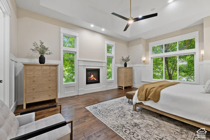 Tray ceiling with integrated recessed lighting, wood-finish flooring, built-in fireplace, wall paneling, and expansive windows