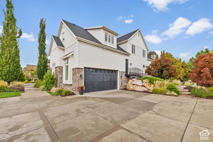 Multi-level exterior featuring white horizontal siding, stone veneer accents, an attached garage with multi-pane windows, and landscaped rock formations