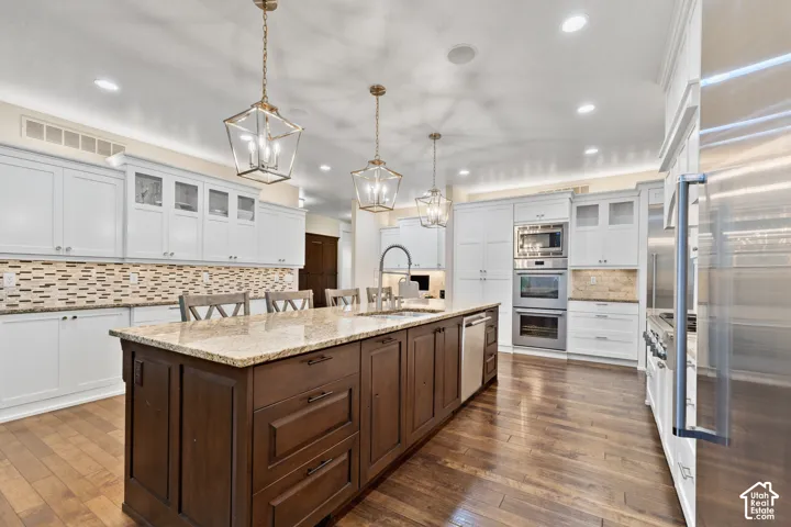 Kitchen featuring a center island with stone countertops, stainless steel double wall ovens, wood-finish flooring, glass-front cabinetry, and pendant lighting