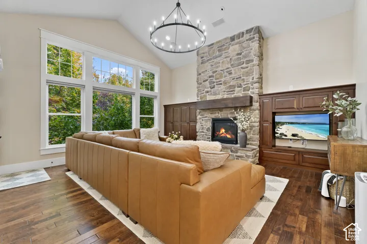 Vaulted ceiling featuring a large-scale wagon wheel chandelier, floor-to-ceiling stone fireplace with a thick timber mantel, and extensive built-in dark wood cabinetry