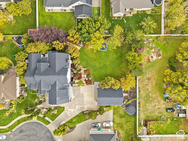Aerial perspective of a multi-gabled roofline, concrete driveway, detached garage, and extensive rear lawn bordered by mature trees and fencing