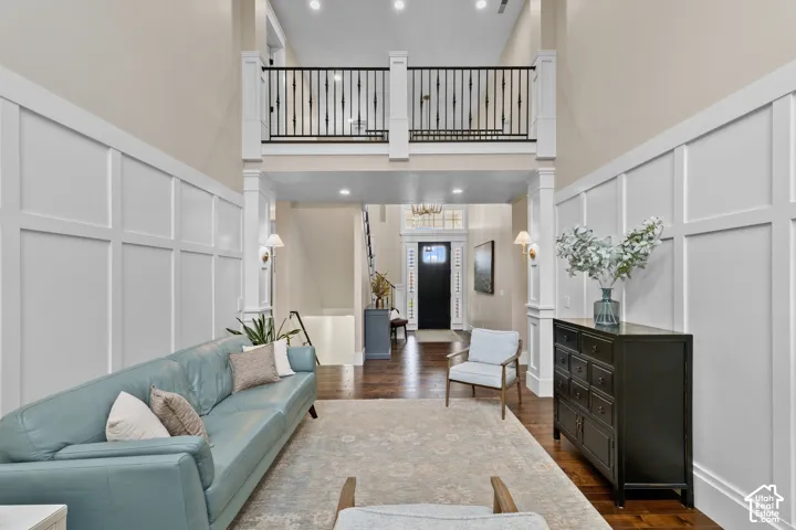 Two-story grand foyer featuring intricate wall paneling, dark wood-finish flooring, a gallery-style metal balustrade, recessed lighting, and a transom-windowed entryway