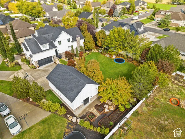 Aerial perspective of a property featuring a white board-and-batten exterior, a detached garage, a concrete driveway, multi-level raised planter beds, and manicured landscaping