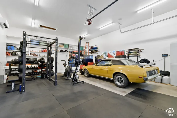 Garage featuring high-output linear LED lighting, concrete flooring with protective matting, built-in wall shelving, and a wall-mounted mini-split climate control unit