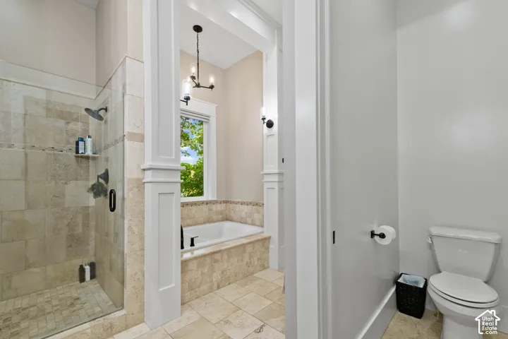 Walk-in shower with stone tile surround, soaking tub with tile deck, decorative millwork columns, and built-in wall lighting fixtures