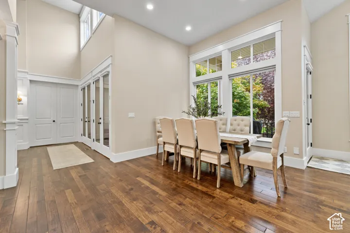 High-ceilinged room featuring wood-finish flooring, recessed lighting, expansive multi-pane windows, and white-framed glass-paneled doors