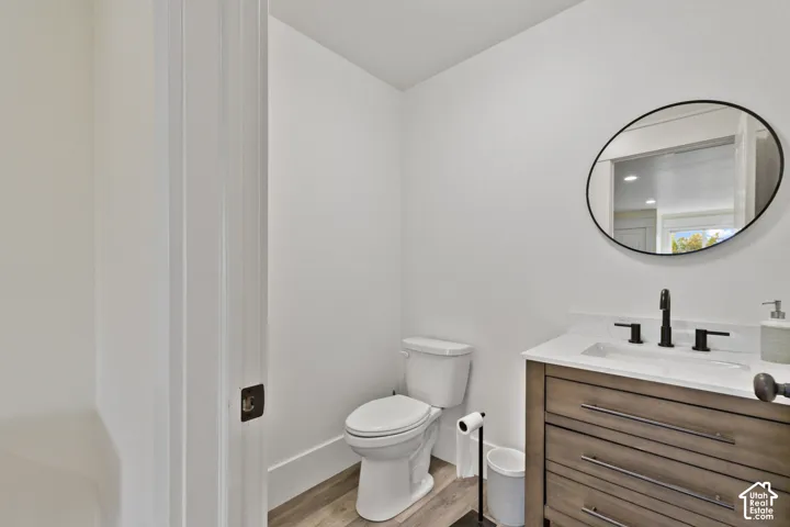 Vanity with wood-finish cabinetry, white countertop, matte black widespread faucet, oval wall-mounted mirror, and wood-finish flooring