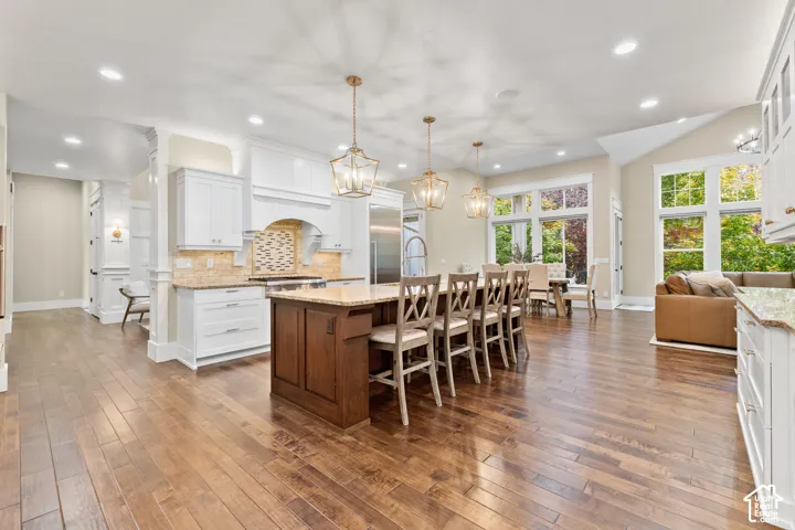 Kitchen featuring wood-finish flooring, a central island with wood cabinetry, white perimeter cabinetry, stone-finish countertops, and multi-light pendant fixtures
