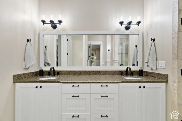 Double vanity featuring white shaker-style cabinetry, dark stone-finish countertops, dual undermount sinks, matte black hardware, and two triple-light wall fixtures