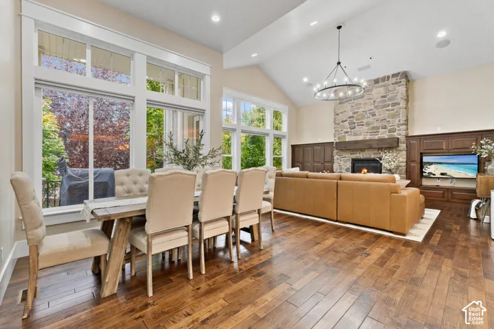 Vaulted ceiling featuring a stone-clad fireplace with a timber mantel, wood-finish flooring, built-in cabinetry, and oversized windows